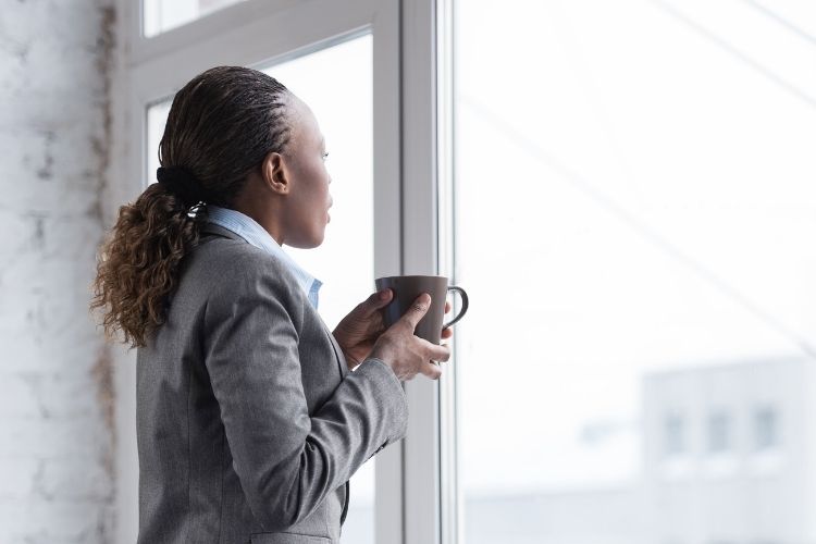 Business woman looking out a window while holding a cup of coffee.