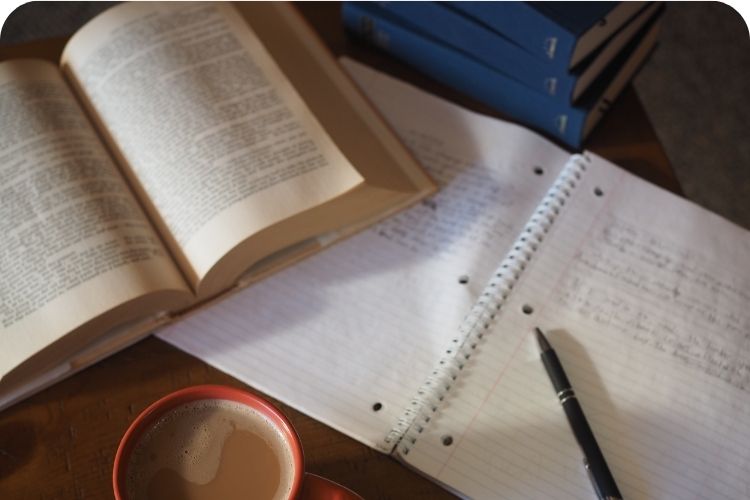 A book, notebook, and cup of coffee sitting on a table.