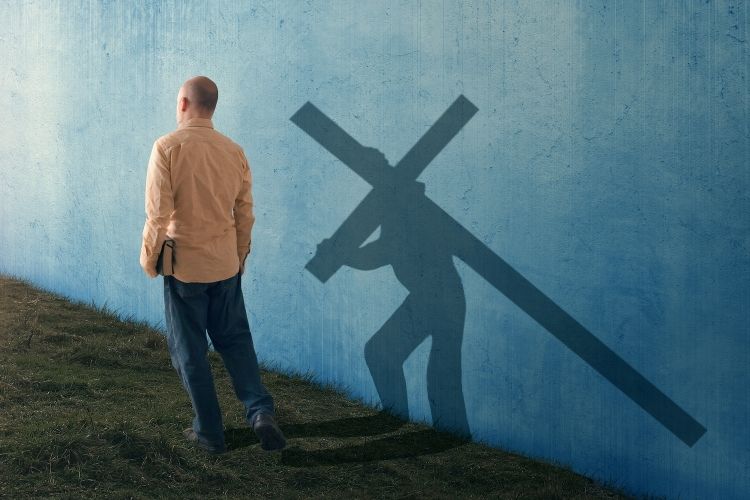 A man carrying his Bible casts a shadow of himself carrying a cross.