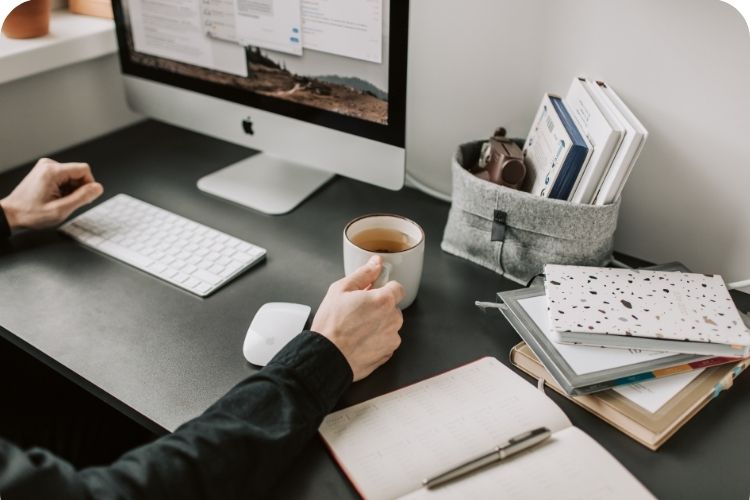 A man siting at his desk working with a full cup of coffee ready to drink.