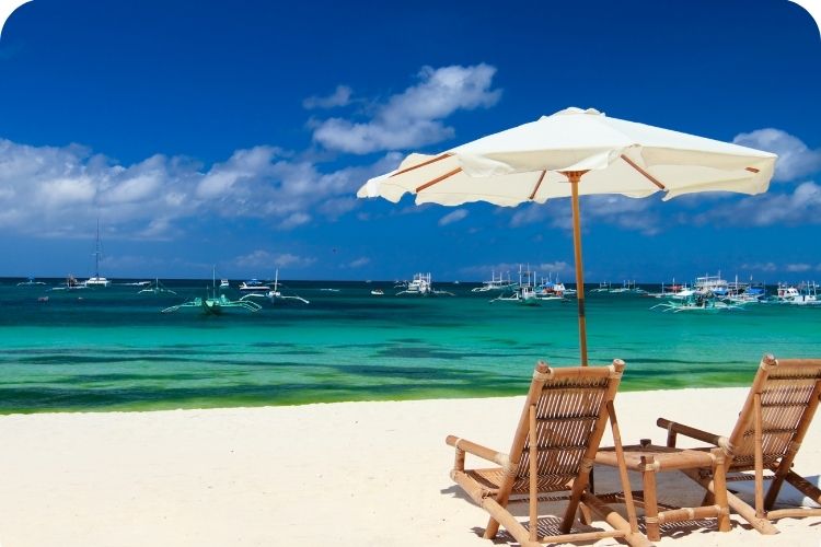 A pristine beach with boats out on the water and lawn chairs on the sand ready to sit in.