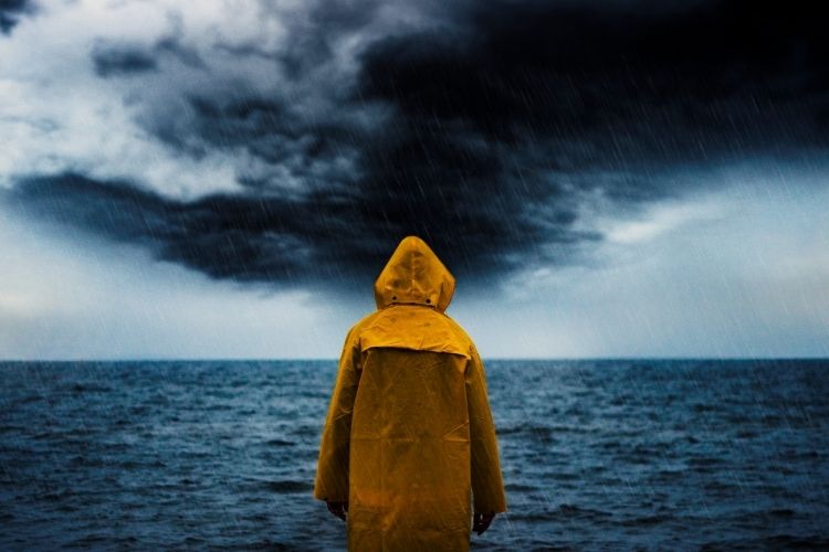 A man standing in front of the ocean as a storm approaches.