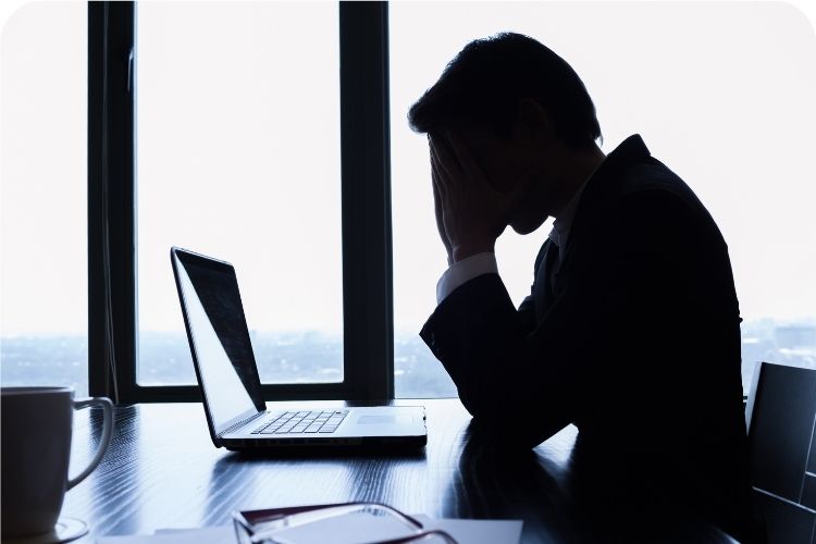 A man sitting at his desk with his head resting in his hands in frustration.
