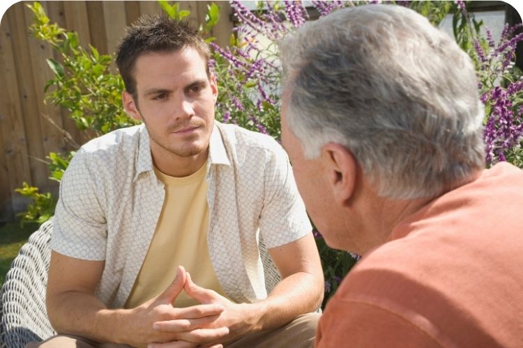 Two men sitting down outside having a serious conversation.