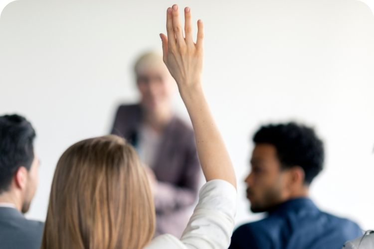 A woman in the audience of a business talk is raising her hand.