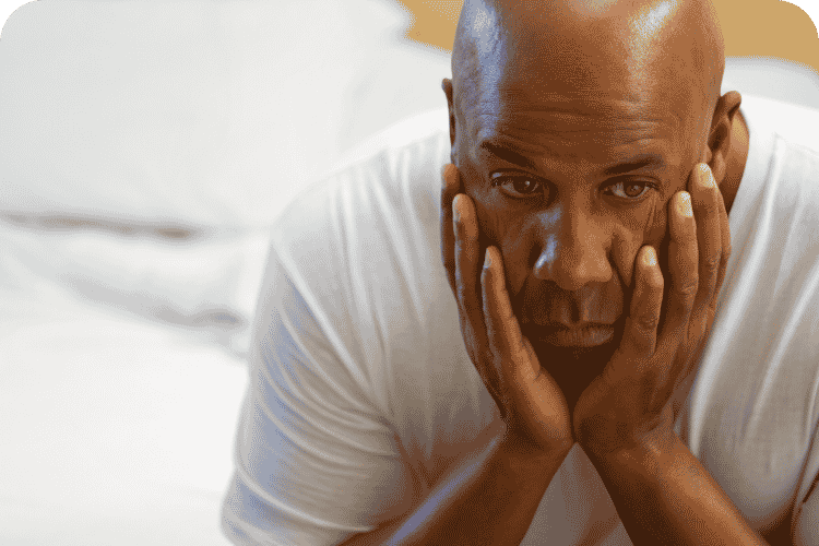 A man sitting on his bed tired.