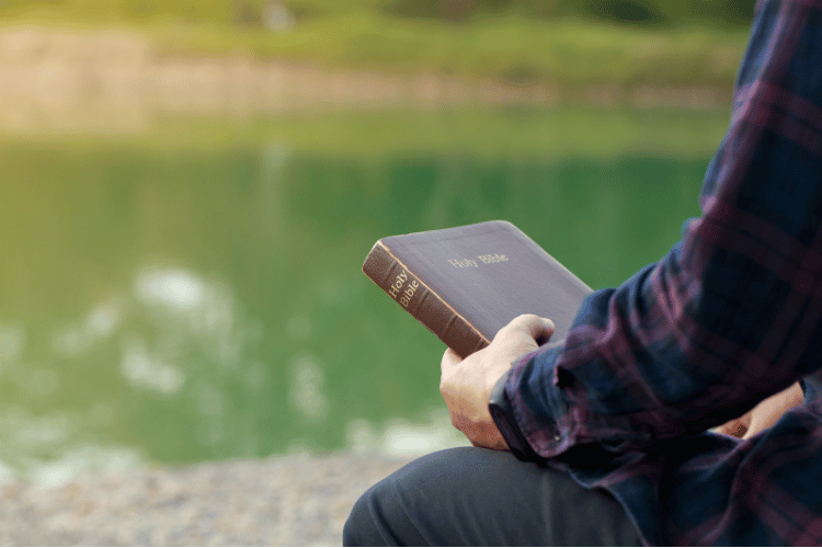 A man sitting by a pond holding his Bible.