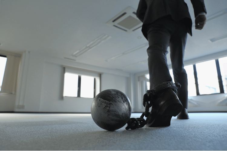 Man in an office building with a ball and chain around his ankle.